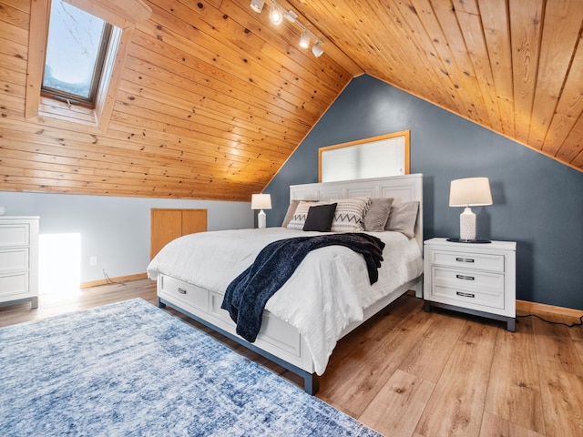 bedroom featuring lofted ceiling with skylight, track lighting, wood finished floors, wooden ceiling, and baseboards