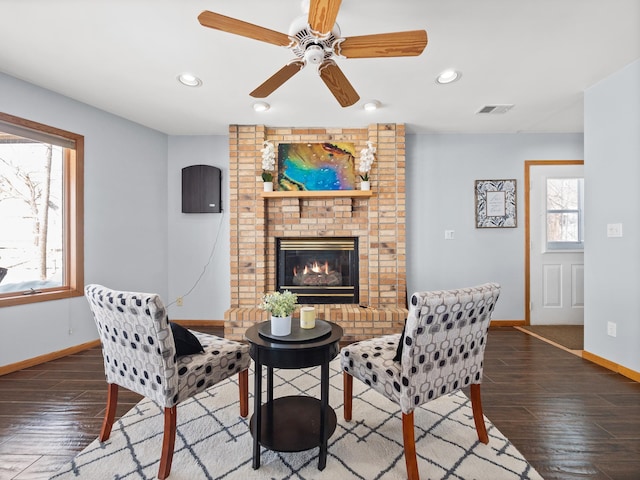 living room with wood finished floors, baseboards, visible vents, recessed lighting, and a brick fireplace