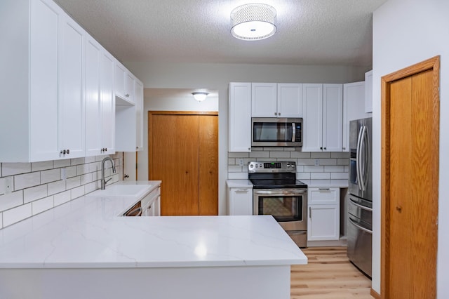 kitchen featuring sink, stainless steel appliances, light stone countertops, white cabinets, and kitchen peninsula