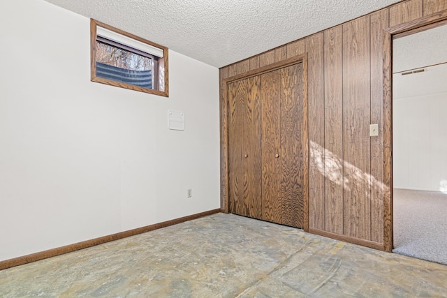 unfurnished bedroom featuring a textured ceiling, wood walls, a closet, and baseboards