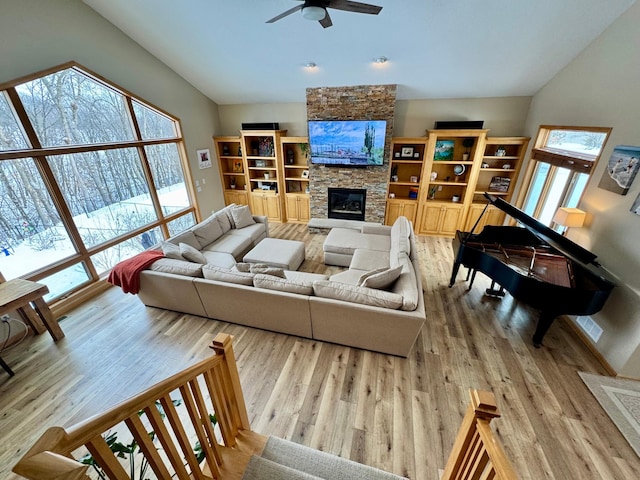 living area featuring a wealth of natural light, ceiling fan, a stone fireplace, and wood finished floors