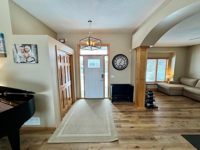 entryway with decorative columns, visible vents, arched walkways, wood finished floors, and a textured ceiling