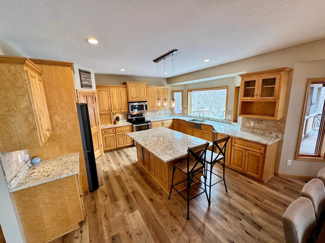 kitchen featuring stainless steel appliances, a breakfast bar area, light wood-style flooring, and pendant lighting