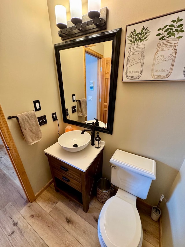 half bath featuring toilet, baseboards, wood finished floors, and vanity