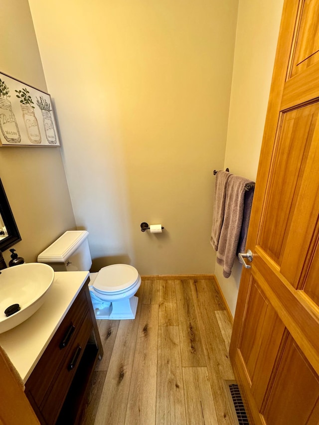 half bathroom with visible vents, toilet, vanity, wood finished floors, and baseboards