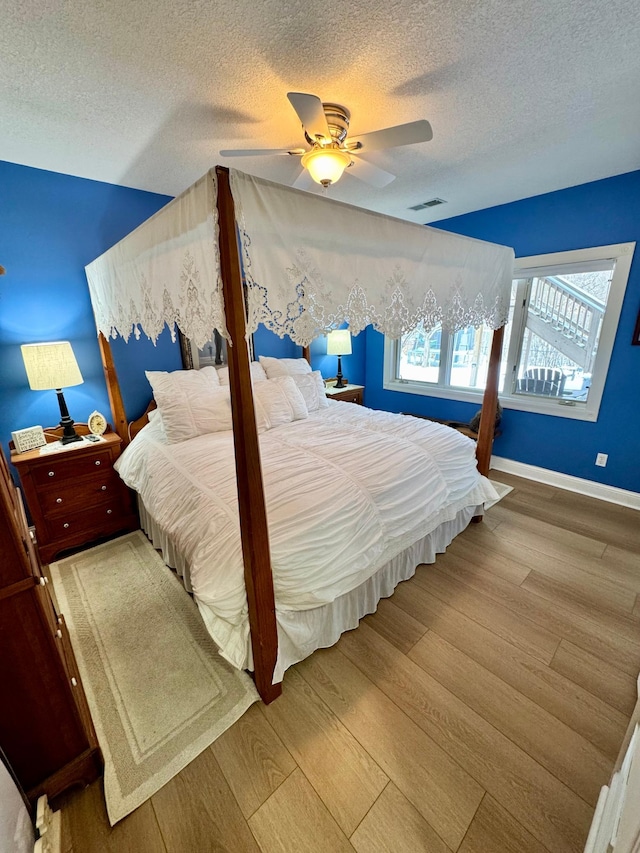 bedroom with baseboards, a textured ceiling, visible vents, and wood finished floors