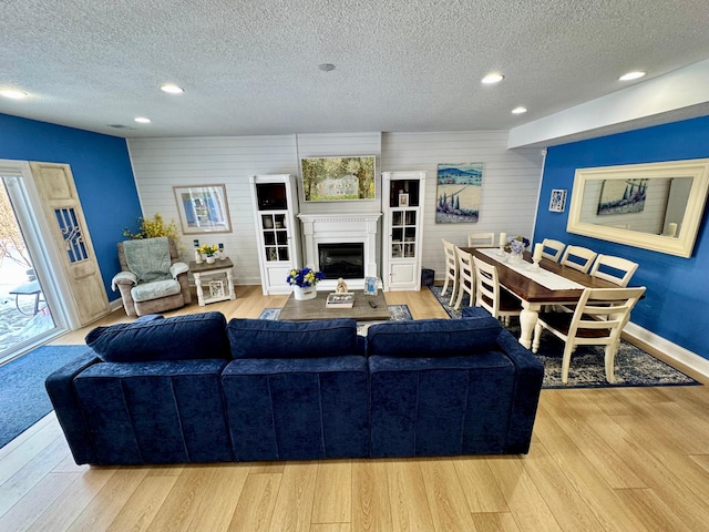 living room with a glass covered fireplace, light wood-style flooring, a textured ceiling, and recessed lighting