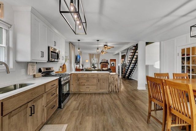 kitchen with a sink, open floor plan, stainless steel appliances, a peninsula, and light wood finished floors