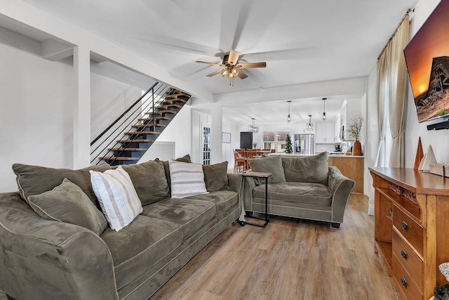 living area featuring stairway, light wood-style flooring, and a ceiling fan