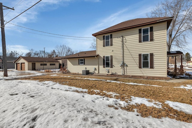 snow covered rear of property featuring a detached garage, central AC unit, and an outdoor structure