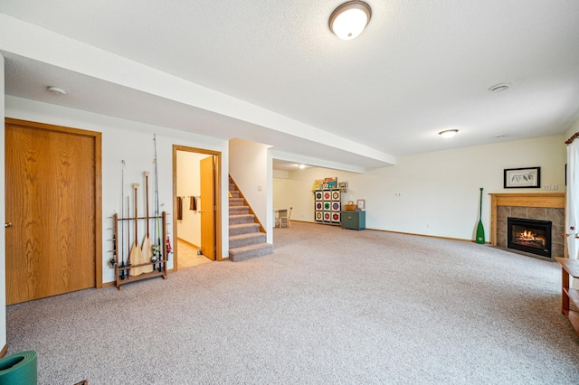 finished basement with a textured ceiling, carpet, stairs, and a tiled fireplace