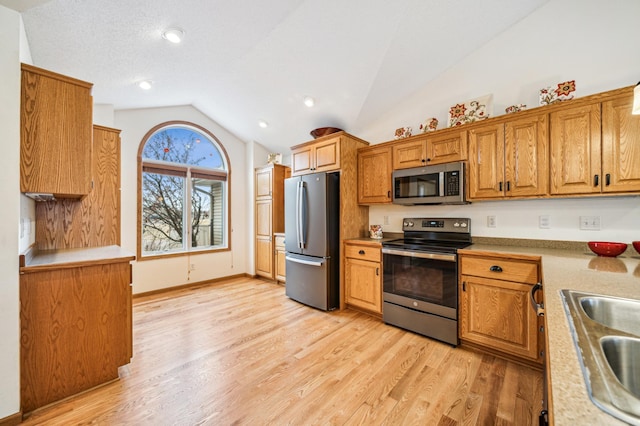 kitchen featuring lofted ceiling, stainless steel appliances, a sink, light wood-style floors, and brown cabinetry