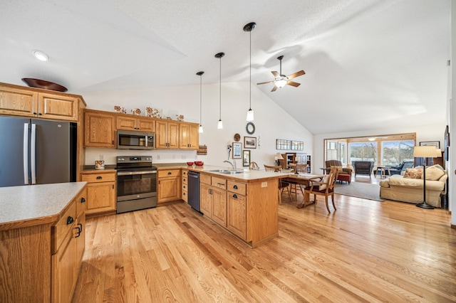 kitchen featuring open floor plan, a peninsula, stainless steel appliances, light wood-type flooring, and a sink