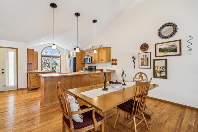 dining area with light wood-style floors, high vaulted ceiling, and baseboards