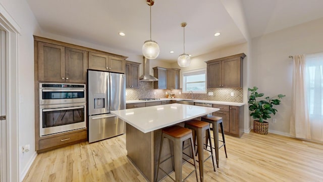 kitchen featuring stainless steel appliances, backsplash, light wood-style flooring, and wall chimney range hood