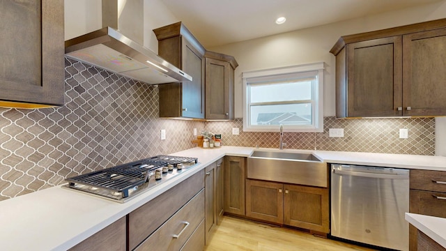 kitchen featuring a sink, light countertops, appliances with stainless steel finishes, wall chimney range hood, and tasteful backsplash