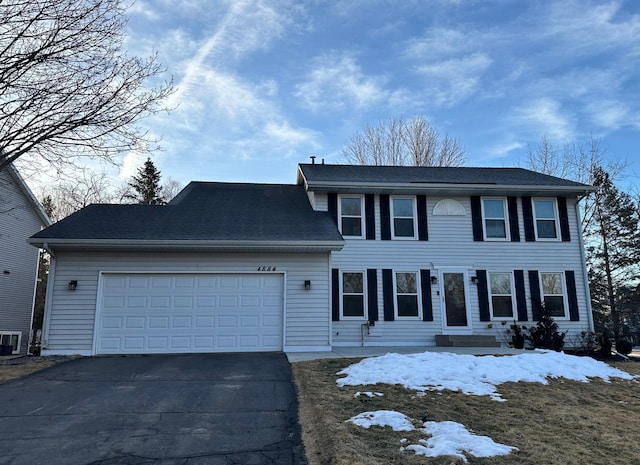 colonial inspired home with an attached garage, driveway, and roof with shingles