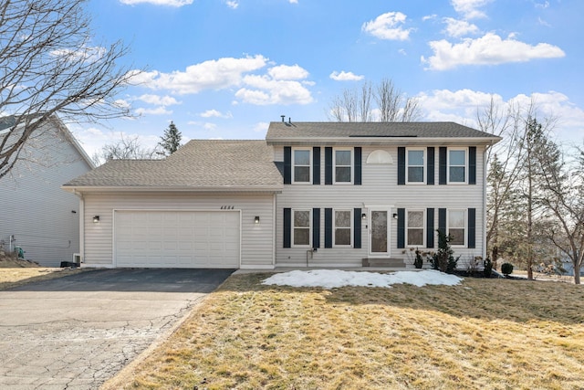 colonial-style house with driveway, a front lawn, an attached garage, and a shingled roof