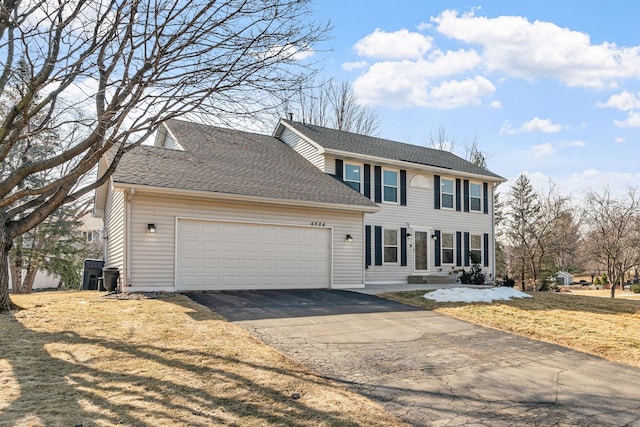 colonial-style house with a front yard, an attached garage, roof with shingles, and driveway