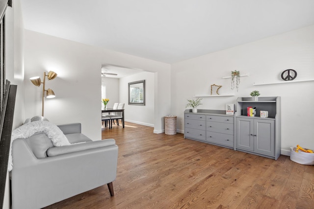 living area with light wood-style flooring, a ceiling fan, and baseboards