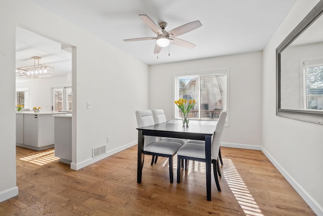 dining area with light wood-type flooring, visible vents, baseboards, and ceiling fan with notable chandelier