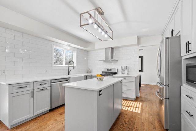 kitchen featuring light wood-style flooring, a sink, decorative backsplash, stainless steel appliances, and wall chimney range hood