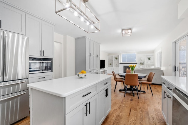 kitchen featuring open floor plan, light countertops, light wood-style flooring, appliances with stainless steel finishes, and white cabinets