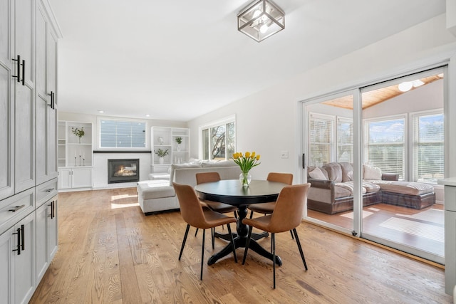 dining area featuring a glass covered fireplace, built in shelves, and light wood-style flooring