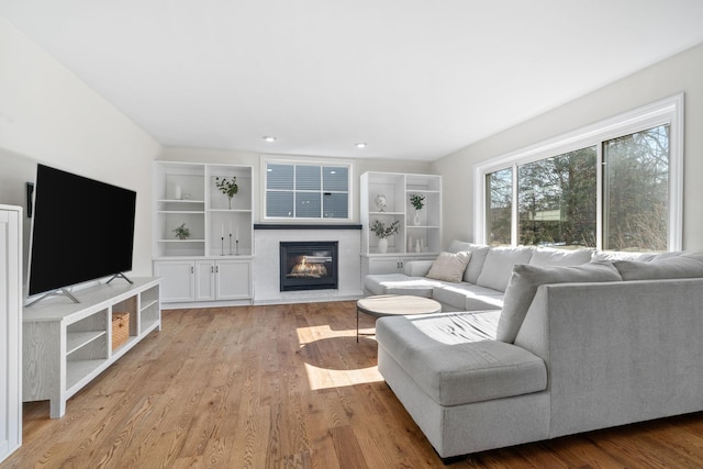 living area with a glass covered fireplace, recessed lighting, and wood finished floors