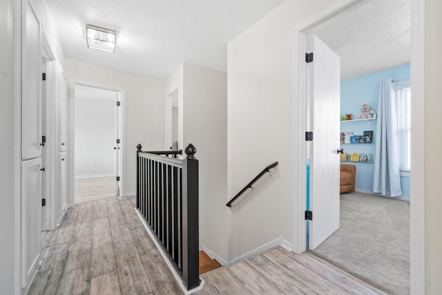 corridor with an upstairs landing, light wood finished floors, a textured ceiling, and baseboards