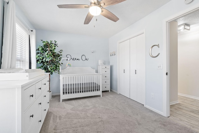 bedroom with baseboards, ceiling fan, light colored carpet, a closet, and a nursery area