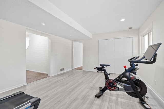 exercise area with wood finished floors, visible vents, and baseboards