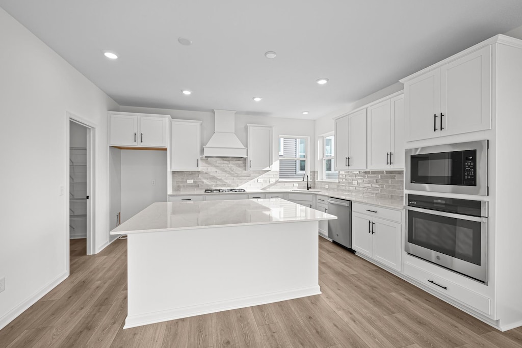 kitchen with stainless steel appliances, a kitchen island, white cabinetry, custom exhaust hood, and light wood finished floors