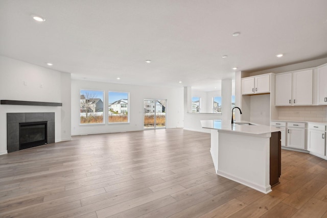 kitchen featuring white cabinetry, sink, a tiled fireplace, a kitchen island with sink, and light hardwood / wood-style floors