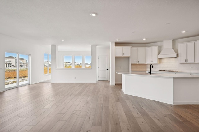 kitchen with tasteful backsplash, white cabinetry, light wood-style floors, and custom range hood