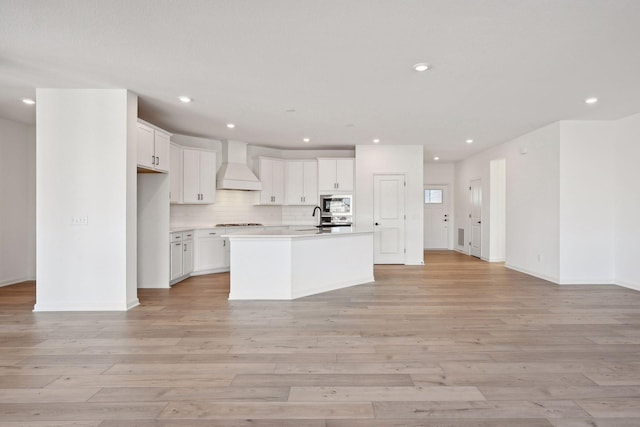 kitchen with a sink, open floor plan, appliances with stainless steel finishes, light wood finished floors, and custom exhaust hood