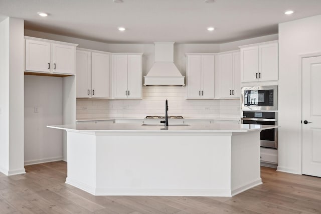 kitchen featuring gas cooktop, custom exhaust hood, a kitchen island with sink, built in microwave, and stainless steel oven