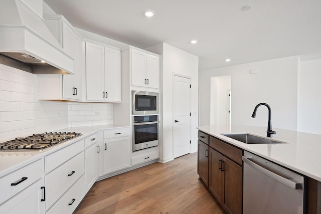 kitchen featuring premium range hood, light wood-type flooring, a sink, stainless steel appliances, and light countertops