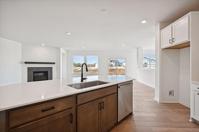 kitchen with a tiled fireplace, dishwasher, light countertops, light wood-style floors, and a sink