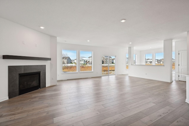 unfurnished living room with a tiled fireplace, recessed lighting, baseboards, and wood finished floors