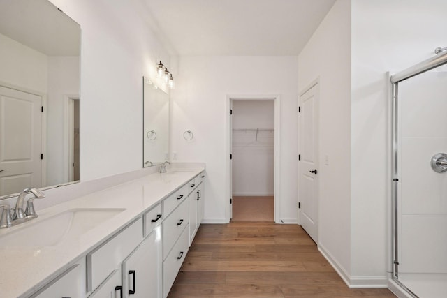 bathroom with double vanity, wood finished floors, a walk in closet, and a sink