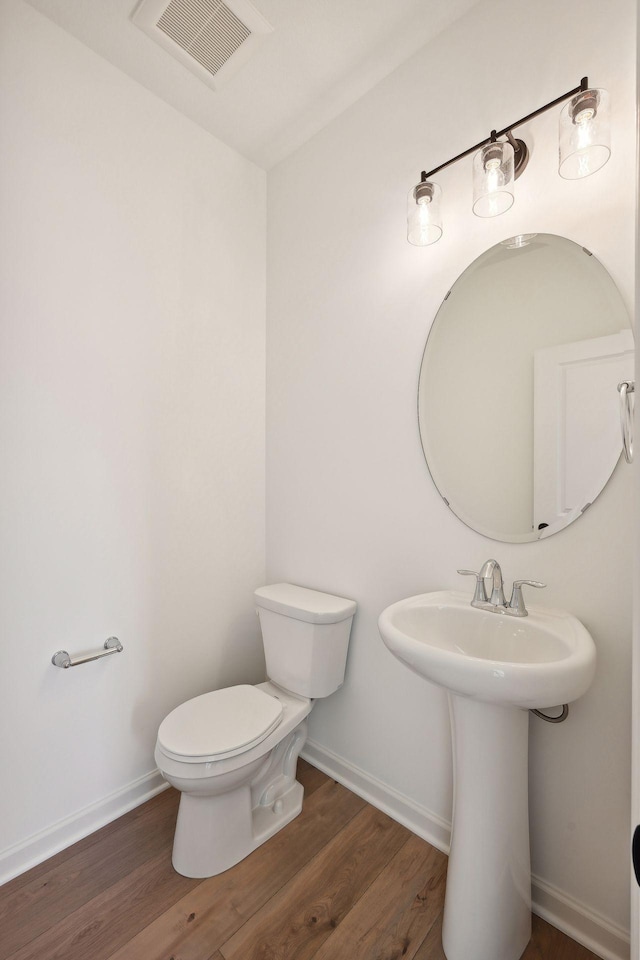 half bathroom featuring visible vents, toilet, wood finished floors, and baseboards