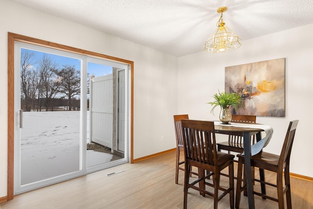 dining area featuring a notable chandelier, light hardwood / wood-style floors, and a textured ceiling