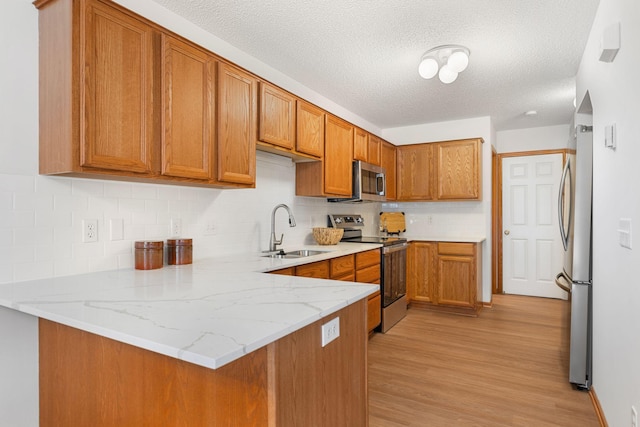 kitchen with light hardwood / wood-style flooring, stainless steel appliances, light stone counters, sink, and kitchen peninsula