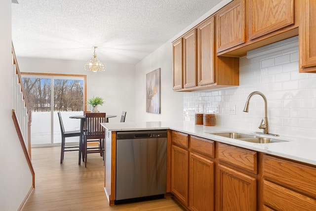 kitchen featuring light hardwood / wood-style flooring, stainless steel dishwasher, decorative light fixtures, sink, and kitchen peninsula