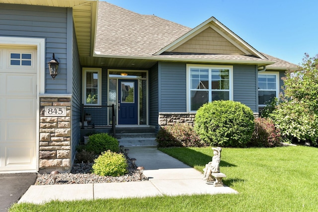 view of exterior entry featuring a garage, stone siding, a shingled roof, and a lawn