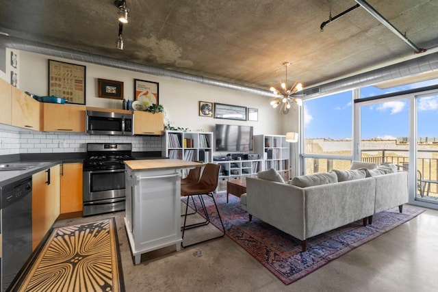 kitchen with concrete flooring, appliances with stainless steel finishes, an inviting chandelier, and decorative backsplash