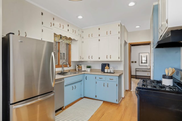 kitchen with under cabinet range hood, light wood-style flooring, stainless steel appliances, blue cabinets, and a sink