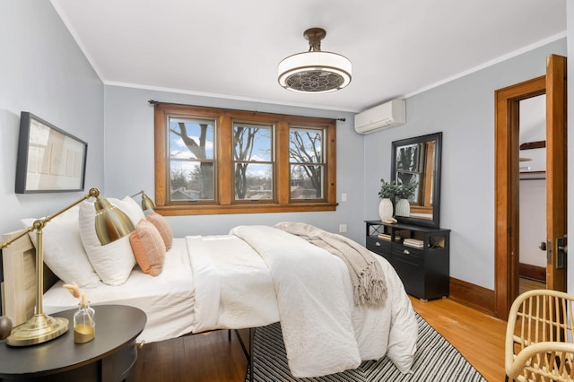 bedroom with a wall unit AC, light wood-style flooring, crown molding, and baseboards