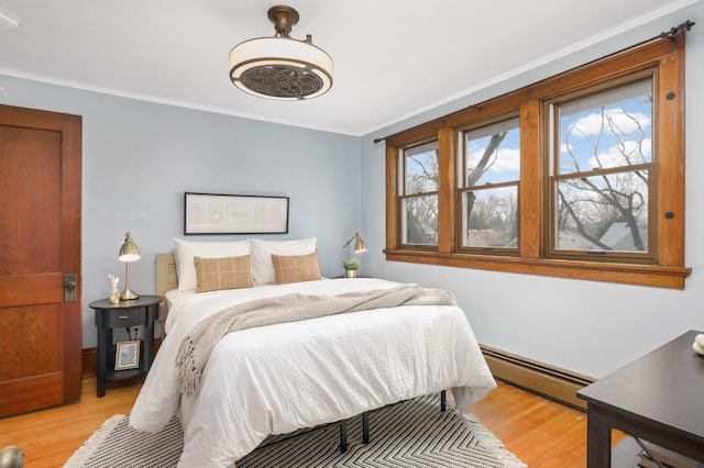 bedroom featuring crown molding, light wood-type flooring, and a baseboard heating unit